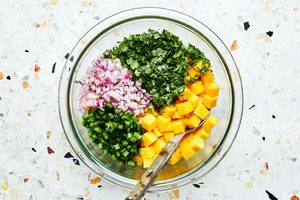 diced mango, red onion, jalapeño, cilantro, and lime juice being tossed in a bowl to make fresh mango salsa