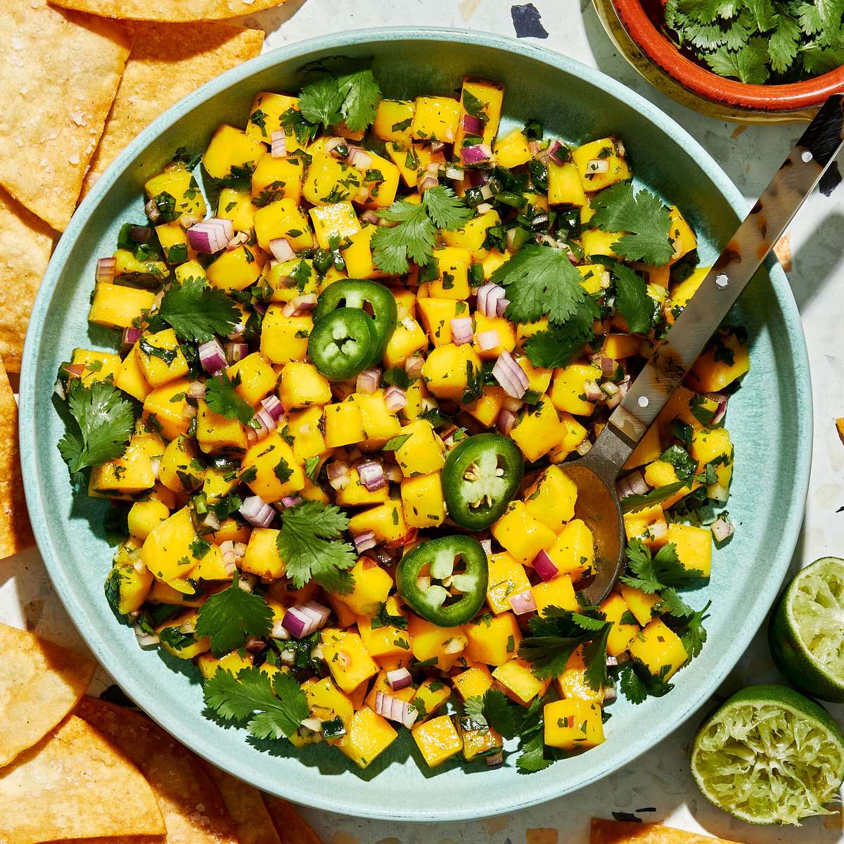 A bowl of fresh mango salsa made with diced mango, red onion, jalapeño, cilantro, and lime juice, served with chips