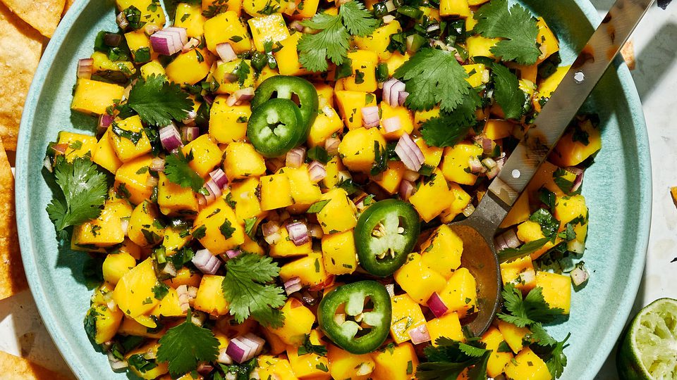 A bowl of fresh mango salsa made with diced mango, red onion, jalapeño, cilantro, and lime juice, served with chips