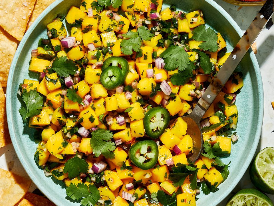 A bowl of fresh mango salsa made with diced mango, red onion, jalapeño, cilantro, and lime juice, served with chips