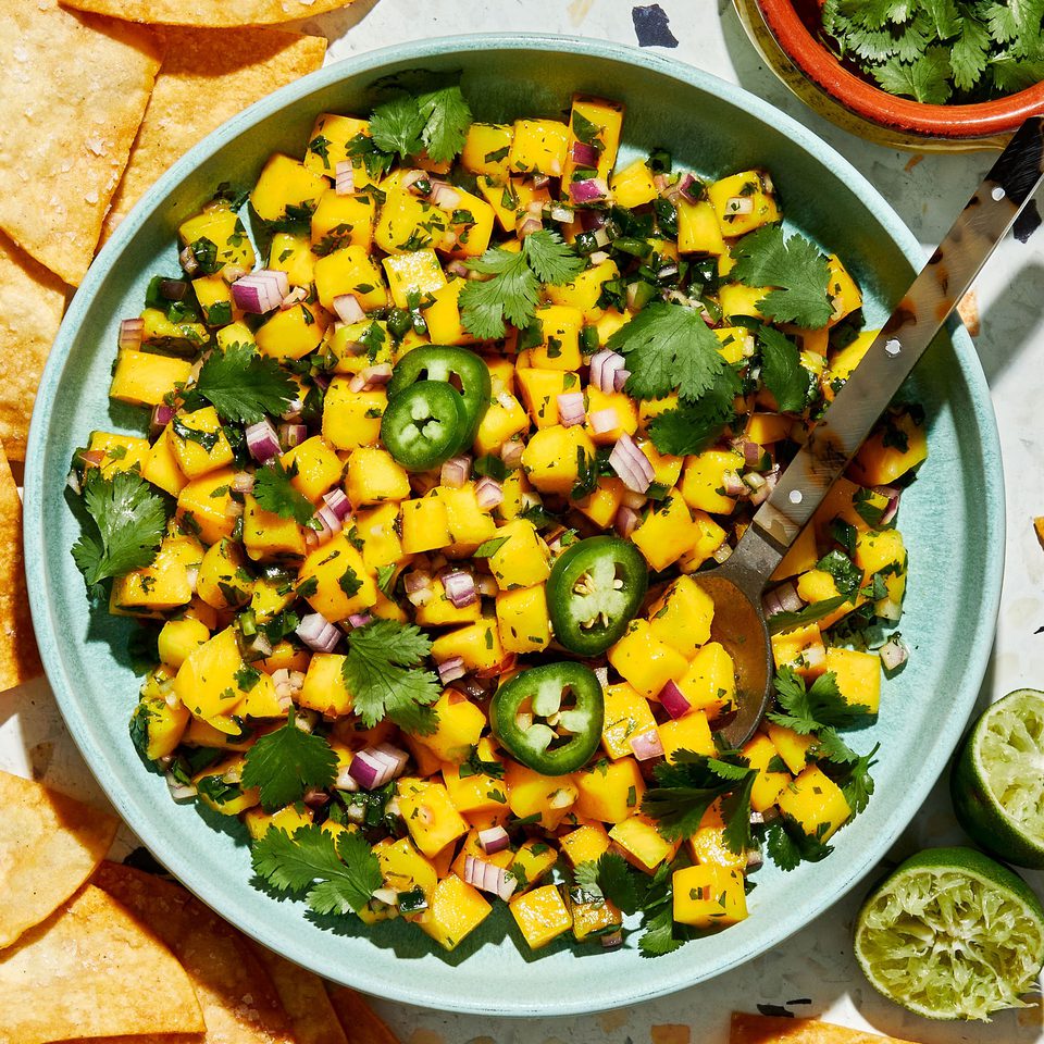 A bowl of fresh mango salsa made with diced mango, red onion, jalapeño, cilantro, and lime juice, served with chips