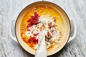 garlic, heavy cream, chicken stock, bouillon, parmesan, sun dried tomatoes and spices being cooked in a skillet