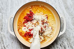 garlic, heavy cream, chicken stock, bouillon, parmesan, sun dried tomatoes and spices being cooked in a skillet
