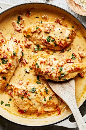 marry me chicken in a pan with a wooden spoon made with cream, chicken stock, chicken bouillon, parmesan, garlic, and spices