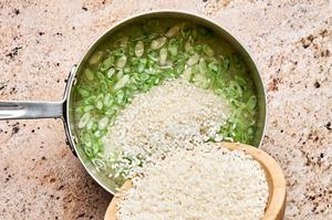 rice being poured in a pot with grated ginger, green onions, water, garlic, and avocado oil in a pot
