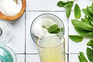 lime juice being poured into a glass with sugar and mint leaves in it to make a mojito