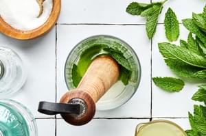 mint leaves, sugar and lime juice being muddled in a glass to make a mojito