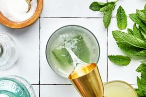 rum being poured into a glass with lime juice, sugar, and muddled mint to make a mojito