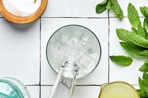 soda water being poured into a mojito with ice to top it off