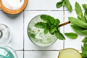 A mojito over ice made with lime juice, sugar, mint, rum and soda water garnished with fresh mint leaves and lime wedge