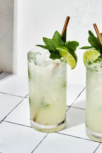 2 Mojitos over ice made with lime juice, sugar, mint, rum and soda water garnished with fresh mint leaves and lime wedge