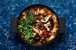 peas being added to mushroom stew being cooked in a pot made with mushrooms, potatoes, spices, wine and vegetable stock