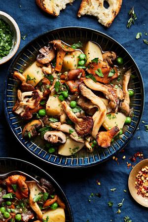 a bowl of homemade mushroom stew made with mushrooms, potatoes, peas, and onions served with crusty bread