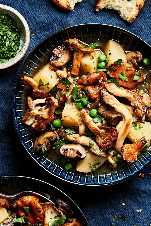 a bowl of homemade mushroom stew made with mushrooms, potatoes, peas, and onions served with crusty bread
