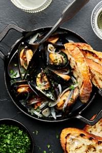 a pot of mussels in wine sauce served with crusty bread