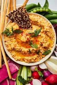 homemade nutty carrot dip in a bowl on top of a platter surrounded with raw peas, cucumbers, radishes and crackers