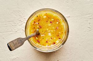 homemade orange vinaigrette in a dish with a spoon made with vinegar, olive oil orange juice, dijon, shallots, salt & pepper