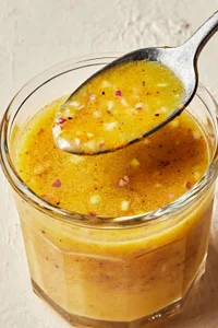 homemade orange vinaigrette in a dish with a spoon made with vinegar, olive oil orange juice, dijon, shallots, salt & pepper