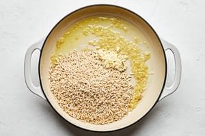 shallots, orzo and garlic being cooked in olive oil in a pot making orzo risotto