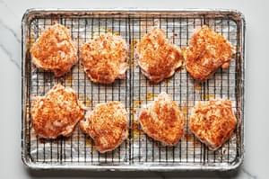 seasoned chicken thighs on a wire cooling rack on top of a foil lined baking sheet ready to be baked in the oven