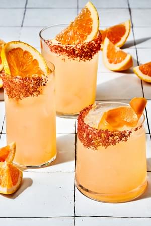 three homemade Palomas in a salt rimmed glasses over ice garnished with grapefruit wedges with extra wedges on the counter