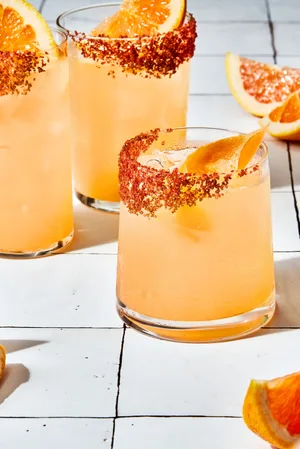 three homemade Palomas in a salt rimmed glasses over ice garnished with grapefruit wedges with extra wedges on the counter