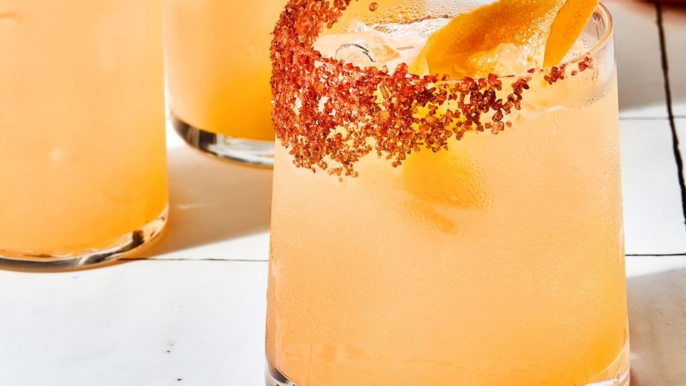 three homemade Palomas in a salt rimmed glasses over ice garnished with grapefruit wedges with extra wedges on the counter