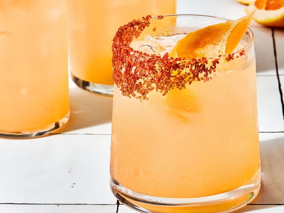 three homemade Palomas in a salt rimmed glasses over ice garnished with grapefruit wedges with extra wedges on the counter