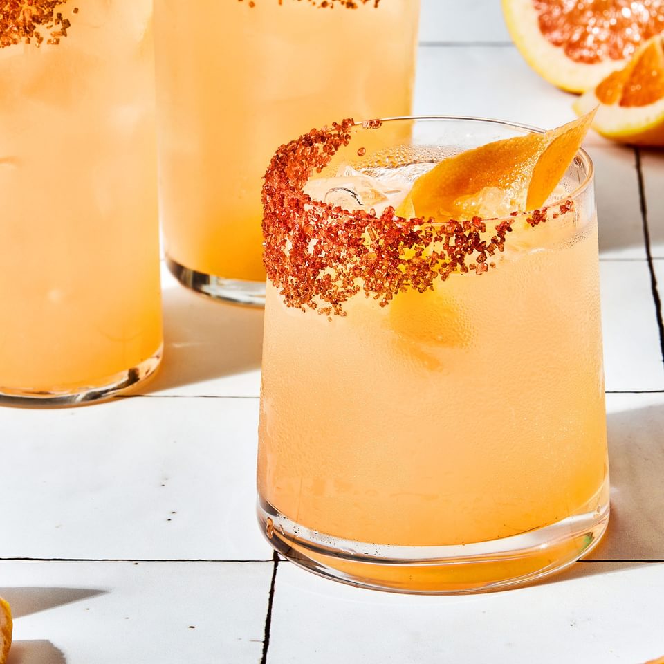 three homemade Palomas in a salt rimmed glasses over ice garnished with grapefruit wedges with extra wedges on the counter