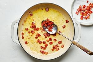 diced guanciale that has been cooked in olive oil being scooped out of a skillet for homemade pasta carbonara
