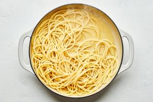 cooked spaghetti noodles being stirred in a skillet with rendered guanciale fat and reserved pasta water