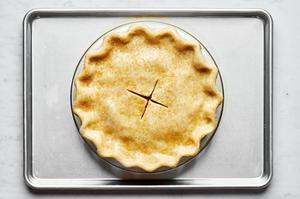 an unbaked peach pie that has been  brushed with egg wash with an x cut on top sit-in non a baking sheet