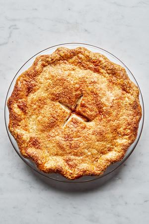 a homemade baked peach pie with brown flaky crust and sprinkled with raw sugar on top