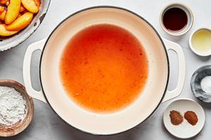 peach juices in a pot surrounded by vanilla, lemon juice, nutmeg, cinnamon, salt and cornstarch to make a peach pie filling