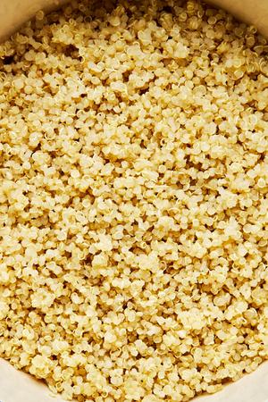 a close up view of perfectly cooked, fluffy, white quinoa in a small sauce pan being fluffed with a fork