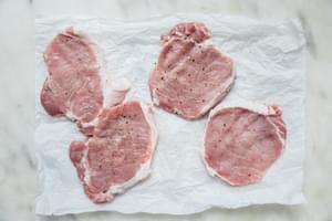 pounded pork chops seasoned with salt and pepper on parchment paper ready to be dredged for homemade pork schnitzel