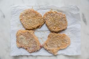 pounded pork chops dredged in flour, egg and plain breadcrumbs on parchment paper ready to be fried for pork schnitzel