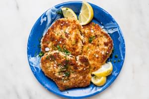 homemade pork schnitzel made with salt, pepper, flour, egg and plain breadcrumbs on a plate with lemon wedges for serving