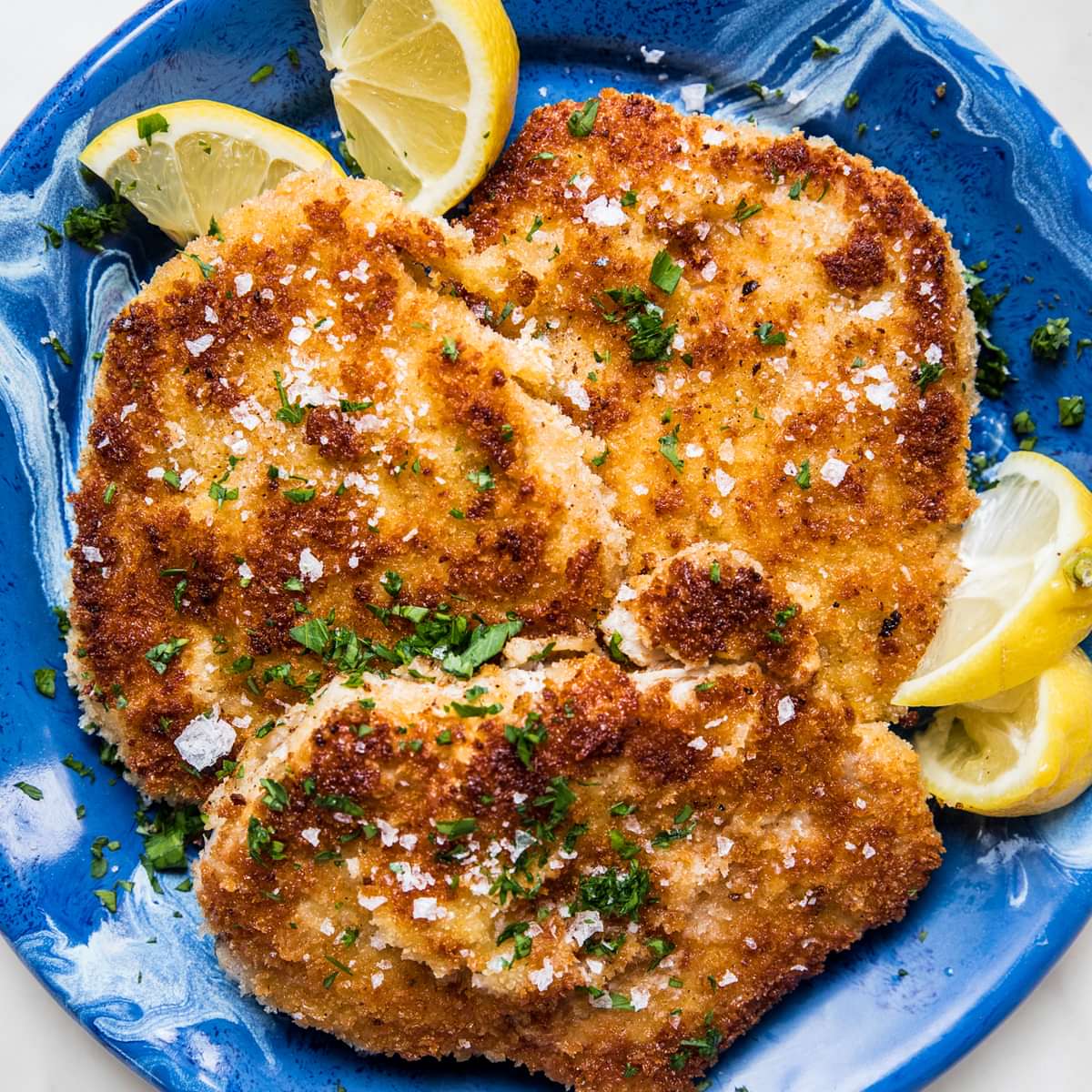 homemade pork schnitzel made with salt, pepper, flour, egg and plain breadcrumbs on a plate with lemon wedges for serving