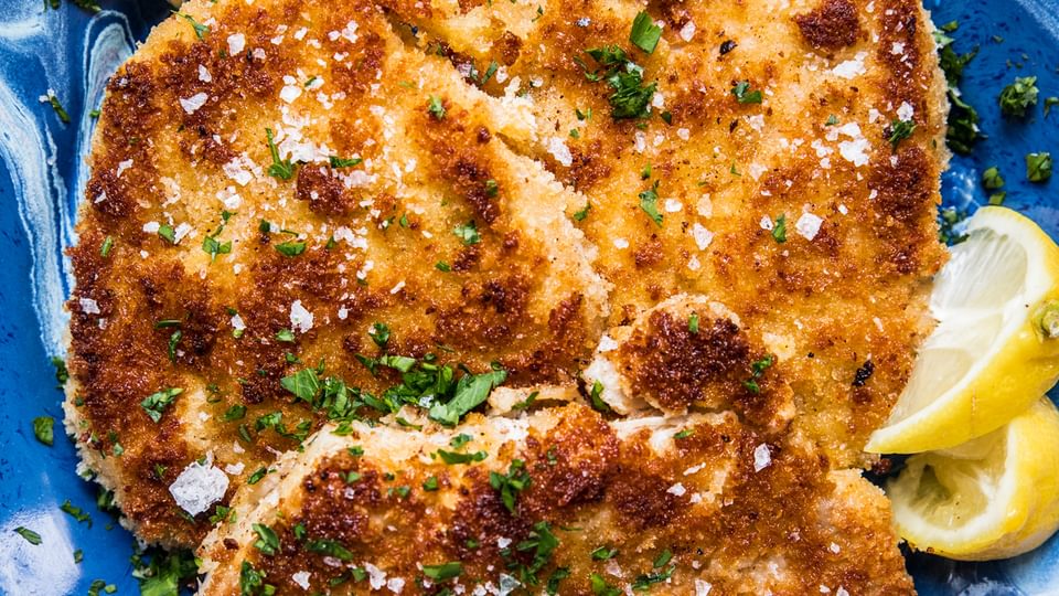 homemade pork schnitzel made with salt, pepper, flour, egg and plain breadcrumbs on a plate with lemon wedges for serving