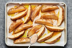 raw potato wedges on a parchment lined baking sheet drizzled with olive oil and being sprinkled with a homemade spice mix