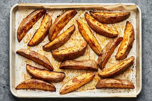 raw potato wedges on a parchment lined baking sheet tossed with olive oil, brown sugar, salt, pepper, paprika & garlic powder