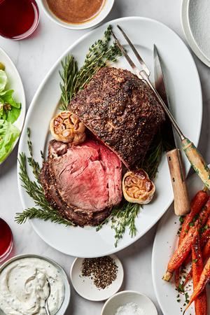 homemade prime rib sliced on a serving plate being served with roasted garlic and horseradish cream sauce