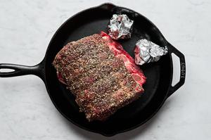 a seasoned prime rib in a cast iron skillet with heads of garlic wrapped in foil