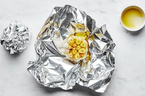 garlic heads with the tops trimmed off and drizzled with olive oil being wrapped in foil