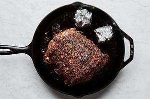a seasoned prime rib in a cast iron skillet with heads of garlic wrapped in foil