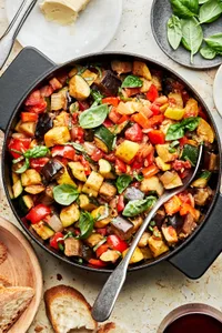 homemade ratatouille in a pot with a spoon made with diced vegetables, spices, olive oil and fresh basil