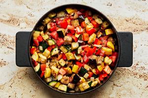 onion, garlic, thyme, tomatoes and bell peppers being cooked in olive oil in a skillet