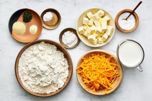 flour, butter, baking powder, baking soda, shredded cheddar cheese, whole milk and spices in bowls on the counter