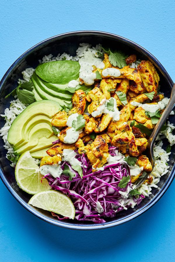 A rice bowl with turmeric ginger chicken, avocado, red cabbage, lime wedges and cilantro ranch